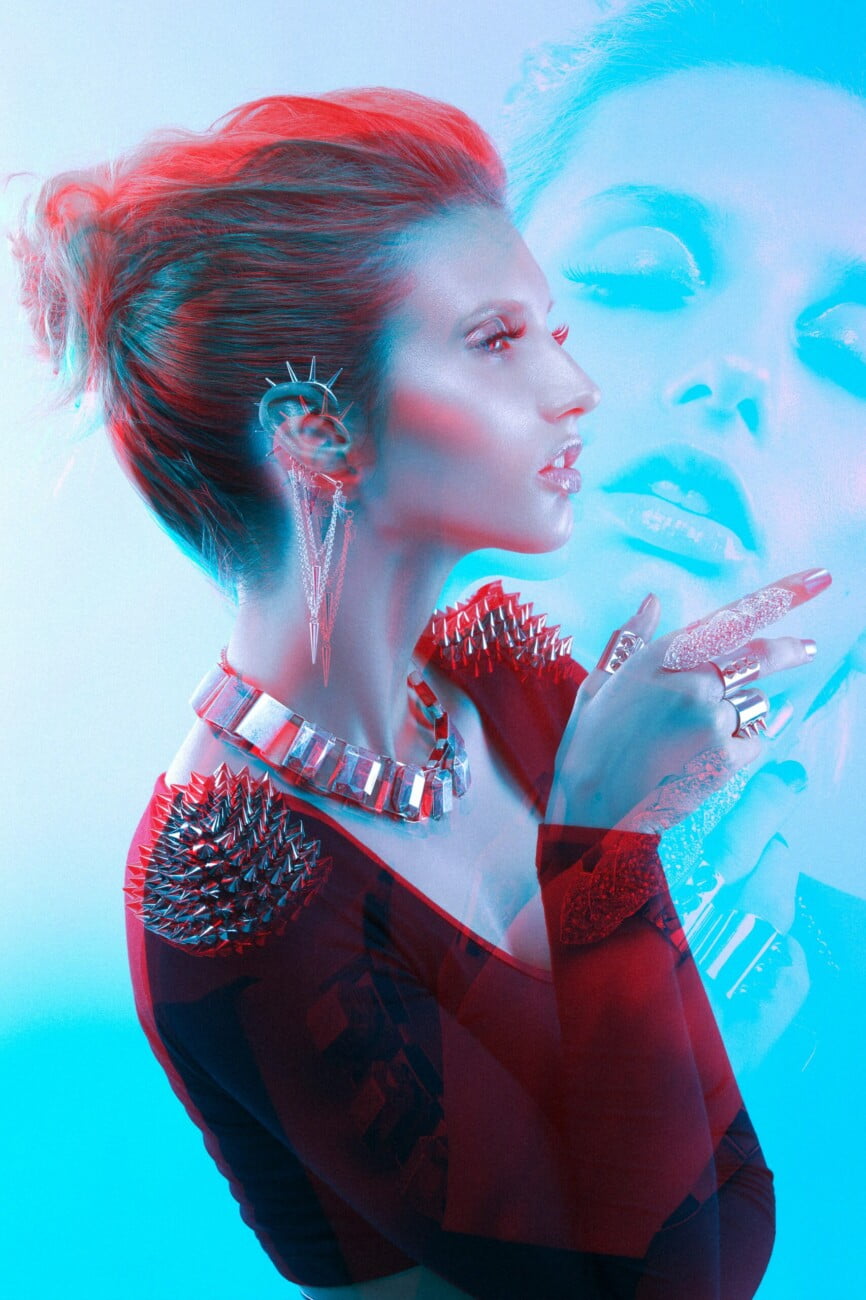 Graphic portrayal of model Adeline Petit in elegant attire with exquisite jewelry, captured in an electric blue and red artistic image by photographer Etienne Delorme for Faust Magazine.